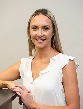 portrait of Tayla smiling professionally - a young woman with dark blond hair wearing a white top