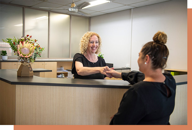 woman with curly hair smiling and shaking hands with female client in black top over reception desk