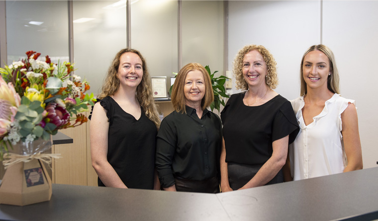 rachel, Sue, Lorraine and Tayla standing behind reception desk smiling professionally